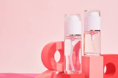 Pembe arka planda pembe bir kürsüde iki cam şişe parfüm şişesi ya da serum kozmetik şişeleri. Kimlik modelleme konsepti.