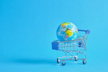 Mavi arka planda süpermarket alışveriş arabasında bir dünya gezegeni. Dünya gezegeni şeklinde uzay alışveriş arabalarını ve oyuncak toplarını kopyala
