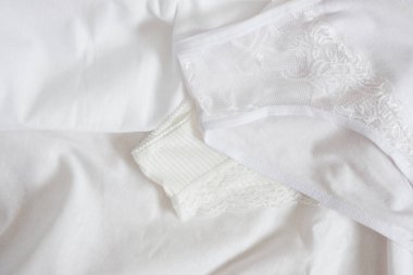 Yatakta iç çamaşırlı kadın. Zarif, beyaz dantelli dantelli külotun beyaz bir bezde yakın plan çekimi. Seçici odak