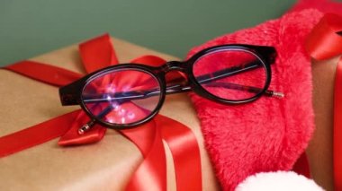 Sanat gözlüğü. Yeşil arka planda kırmızı kurdeleli köknar dalı ve hediye kutuları. Optik mağazada noel alanı indirimi, hediye olarak gözlük.