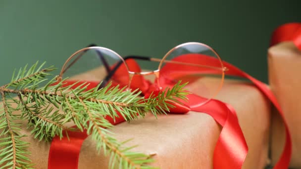 サナッツアイグラス 緑の背景に赤いリボンが付いたモミの枝とギフトボックスコピースペース光店でクリスマスセール ギフトとして眼鏡 — ストック動画