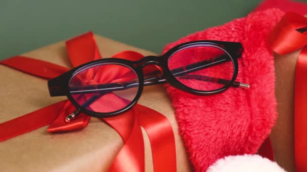 萨纳特眼镜 冷杉分枝和礼品盒 绿色背景上有红丝带 光学商店出售太空圣诞礼物 眼镜作为礼物 — 图库视频影像