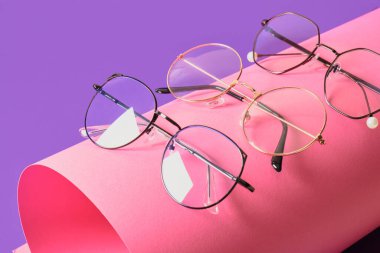 Pembe ve mor geometrik arkaplanda farklı moda gözlük, rulo kağıt ve moda gözlük çerçeveleri boşluk kopyala