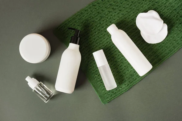 Yeşil arka planda yeşil örülmüş eşarp üzerine beyaz şişeler ve kozmetik ürünler. Güzellik ürünlerinin Noel indirimi konsepti. Boşluğu kopyala