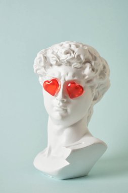 David 'in gözlerinde kırmızı cam kalplerle sahte büstü, aşk konsepti, sevgililer günü. Tebrikler. Açık mavi arka planı kopyala.