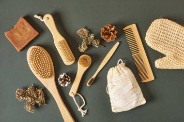 eco friendly body care set on green background top view, homemade soap, wooden massage brushes, bamboo toothbrush and knitted washcloth, winter skin care