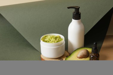 Çukurlu avokado, beyaz model bir kavanozda ev yapımı avokado kozmetik maske ve yeşil arka planda avokado dilimleri olan bir şişe krema. Doğal kozmetik konsepti.