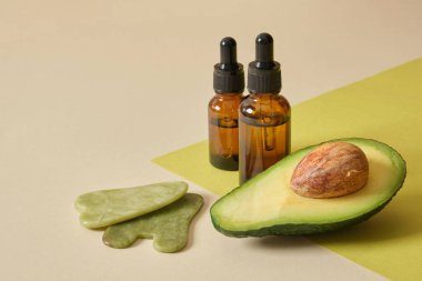 avokado polovieka, kehribar cam düşürücü şişeler ve yeşim taşı kazıyıcılar, avokado yağı ve yeşim taşı masaj spatulasıyla yüz ve vücut masajı