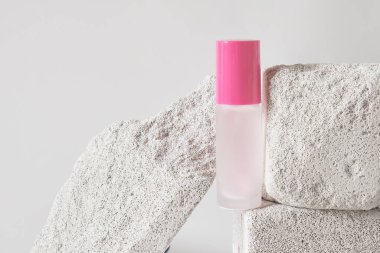 Gri arka planda yapay taş sahnede şeffaf bir parfüm şişesi. Kadın ve erkeğin özünü. Kısa ve öz parfüm şişeleri