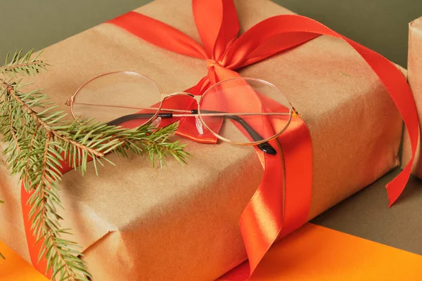 红色缎带礼品盒上的时髦眼镜盒 圣诞视光商店 圣诞老人眼镜和冷杉分枝绿色和橙色背景 — 图库照片