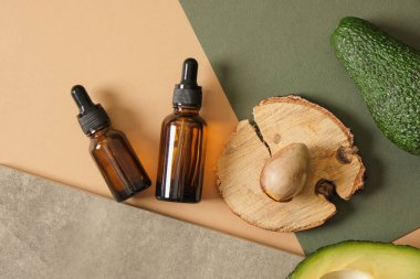 Dilimlenmiş avokado, avokado tohumu ve ahşap bir tezgahın üzerinde iki kehribar cam damlası şişesi yeşil arka plan manzarası doğal kozmetik konsepti