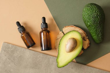 Dilimlenmiş avokado, avokado tohumu ve ahşap bir tezgahın üzerinde iki kehribar cam damlası şişesi yeşil arka plan manzarası doğal kozmetik konsepti