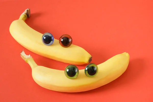 two banana face with eyes, cheerful faces made of plastic doll eyes and fresh yellow bananas red background 14 february concept