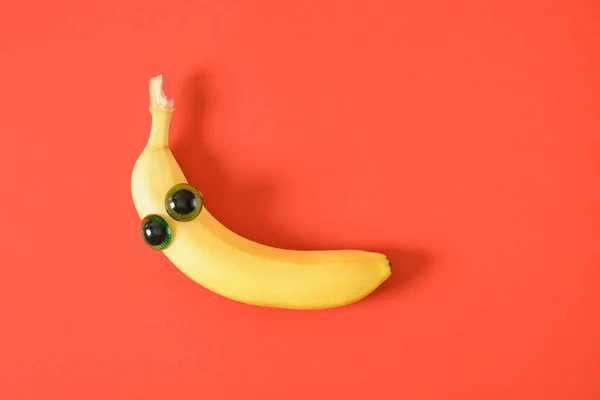 banana face with eyes, cheerful face made of plastic doll eyes and fresh yellow banana red background