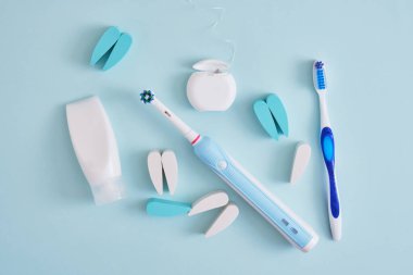 Diş macunu, diş ipi, elektrikli ve plastik diş fırçaları mavi arka planda, diş fırçaları ağız boşluğunu temizlemede daha etkili ve çevre dostu.