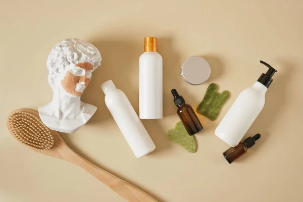 a copy of the antique sculpture of David with a mask of cosmetic clay on his face, massage products and various mock up bottles of cosmetics on a beige background