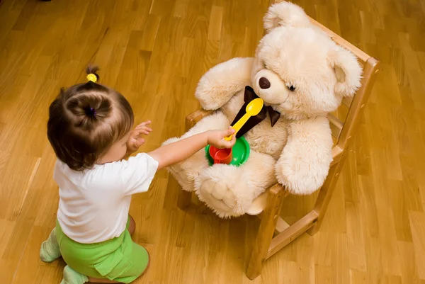 Bambina che gioca con un orso giocattolo e cose da tè — Foto Stock