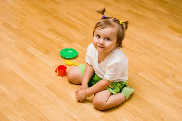 Petite fille assise sur le sol avec des jouets de thé choses — Photo