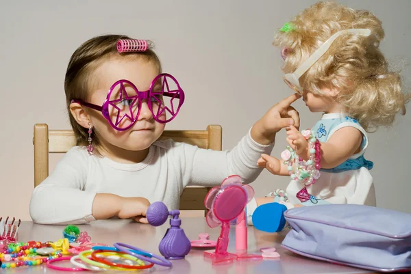 Pequena menina adorável brincando com boneca e óculos de sol de brinquedo — Fotografia de Stock