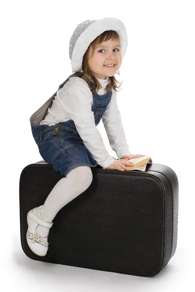 Uśmiechnięta dziewczynka siedzi na walizkę z mała książka — Zdjęcie stockowe