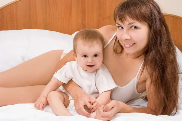 Lyckligt barn och mamma bär vit klädsel spelar i sängen — Stockfoto