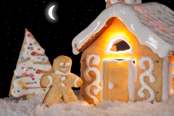 Gingerbread man cookie standing in snow beside house — Stock Photo, Image