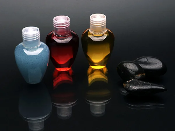 Colorful shampoo set and stones on reflected black surface — Stock Photo, Image