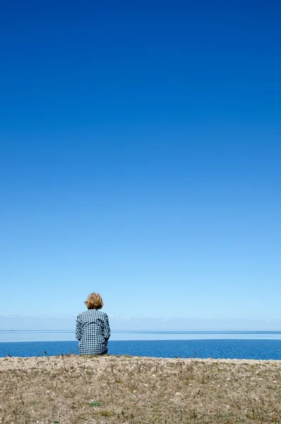 Vertical image of woman sitting by a coast with clear blue and c — Stock Photo, Image