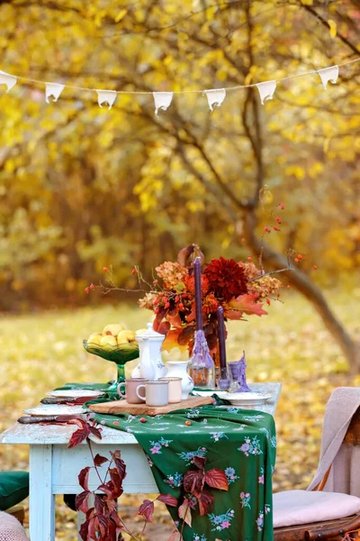 Autumn themed holiday table setting arrangement for a seasonal party, cups, apples, candles, field flowers. Royalty Free Stock Photos