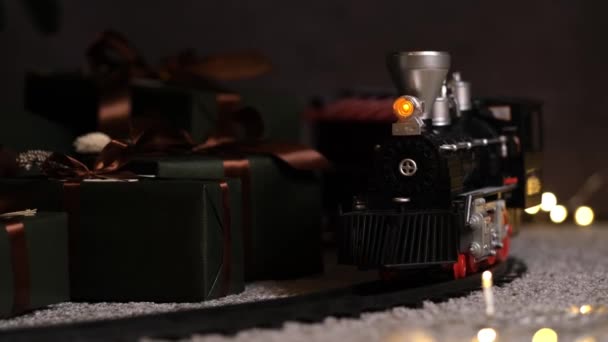 Elegante tren de juguete pasa marcha atrás bajo el árbol de Navidad con muchas cajas de regalo — Vídeo de stock