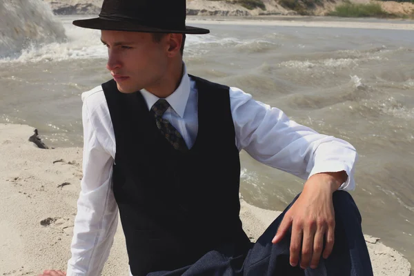 Beautiful brutal man in a classic suit. Cowboy in the desert near the river water. Fashion and Beauty. Black and white in nature — Stock Photo, Image