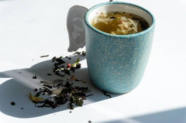 Beyaz arka planda çeşitli otlarla gölgeli bir fincan bitki çayı.