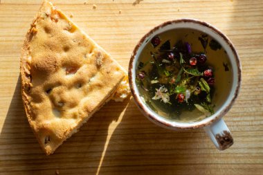 sweet cake with raisins and dried apricots, mug with herbal tea on a wooden board, natural light from the window. Horizontal photo