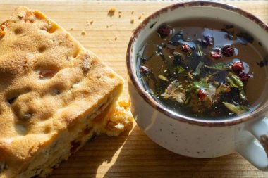 sweet cake with raisins and dried apricots, mug with herbal tea on a wooden board, natural light from the window. Horizontal photo