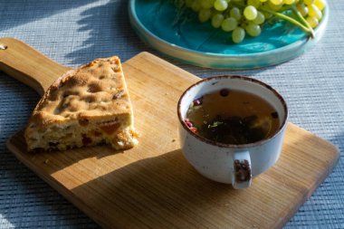 sweet cake with raisins, mug with herbal tea on a wooden board and grapes in the background, natural light from the window. Horizontal photo