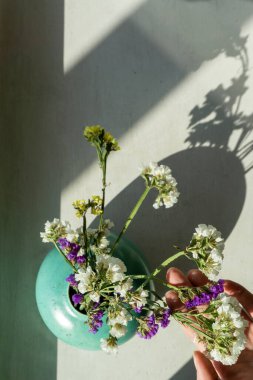 Beyaz masadaki turkuaz seramik vazoda kurumuş çiçekler. Kadın eli. Görünümün üstünde