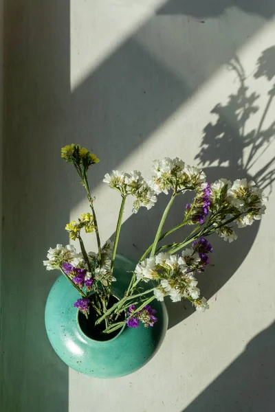 Beyaz masadaki turkuaz seramik vazoda kurumuş çiçekler. Kadın eli. Görünümün üstünde