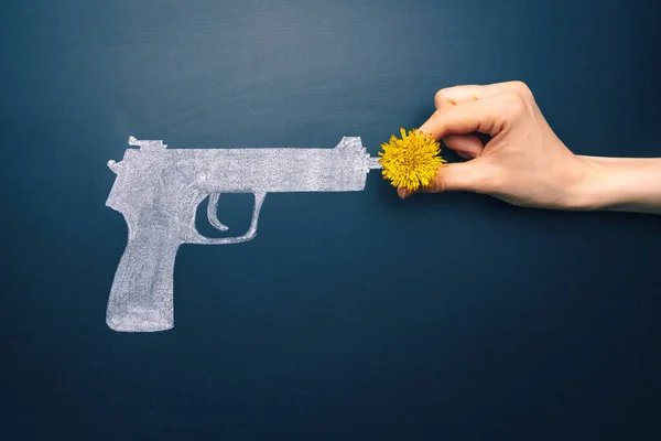 Stop war concept. Not war idea. Gun flower on chalkboard. Girl inserts a flower into a painted gun