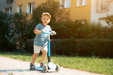 Çocuk güneşli yaz gününde scooter sürmeyi öğreniyor. Çocuk dışarıda scooterla oynuyor. Çocuk için aktif eğlence ve açık hava sporu. Yaz ve çocukluk kavramı.