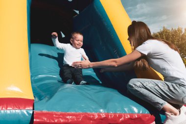 Anne ve oğlu kaydırağın üstünde eğleniyor. Annelik ve çocukluk kavramı. Güneşli yaz günü.