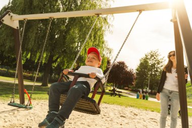 Anne ve oğlu salıncakta eğleniyor. Annelik ve çocukluk kavramı. Güneşli yaz günü.