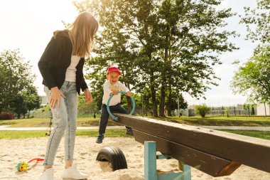 Anne ve oğlu tahterevallide eğleniyor. Annelik ve çocukluk kavramı. Güneşli yaz günü.
