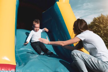 Anne ve oğlu kaydırağın üstünde eğleniyor. Annelik ve çocukluk kavramı. Güneşli yaz günü.