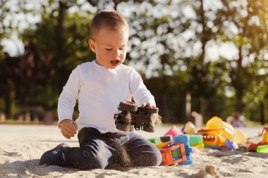 Çocuk kum havuzunda oturup oyuncaklarla oynuyor. Küçük çocuk parkta eğleniyor. Çocuklar için yaz açık hava aktivitesi. Boş zaman yaşam tarzı çocukluğu.