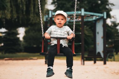 Çocukları salla. Küçük çocuk parkta salıncakta sallanırken eğleniyor. Mutlu çocuk sallanmaktan zevk alır. Şehirde çocuk için aktif açık hava eğlencesi