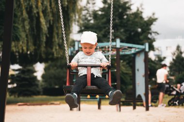Çocukları salla. Küçük çocuk parkta salıncakta sallanırken eğleniyor. Mutlu çocuk sallanmaktan zevk alır. Şehirde çocuk için aktif açık hava eğlencesi