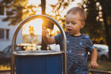 Boy throwing out the trash into a trash bin in summer sunset time. Responsibility, segregated trash, earth day concept.