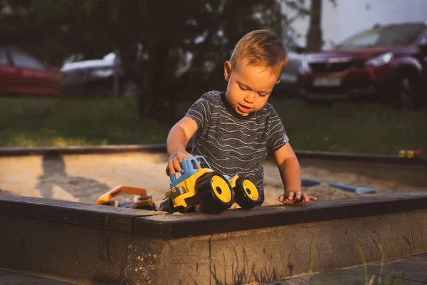 Boy playing with toys in sandbox. Child having fun on playground in sandpit. Outdoor creative activities for kids. Summer and childhood concept.