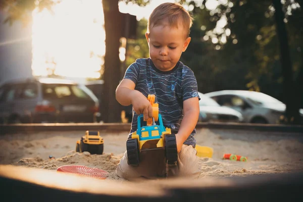 Child playing with toys in sandbox. Little boy having fun on playground in sandpit. Outdoor creative activities for kids. Summer and childhood concept