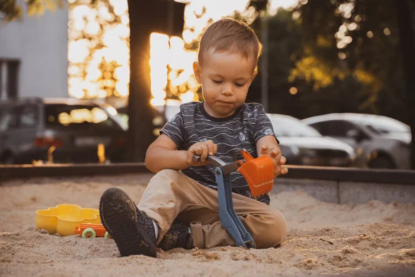 Child playing with toys in sandbox. Little boy having fun on playground in sandpit. Outdoor creative activities for kids. Summer and childhood concept.